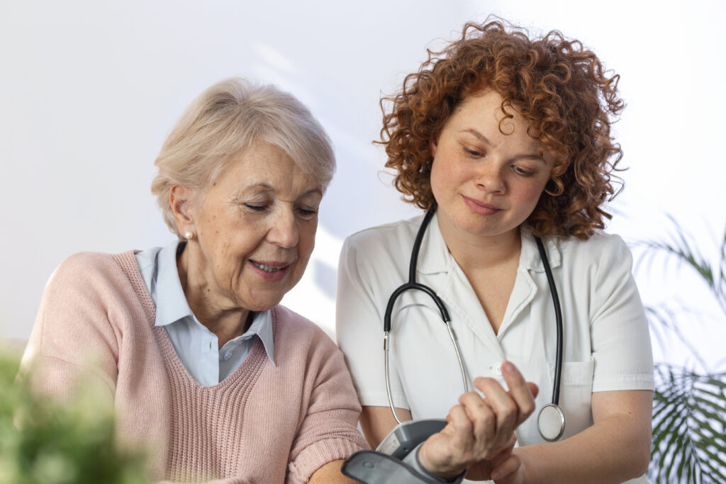 Caregiver measuring blood pressure of senior woman at home. Kind carer measuring the blood pressure of a happy elderly woman in bed in the nursing home.
